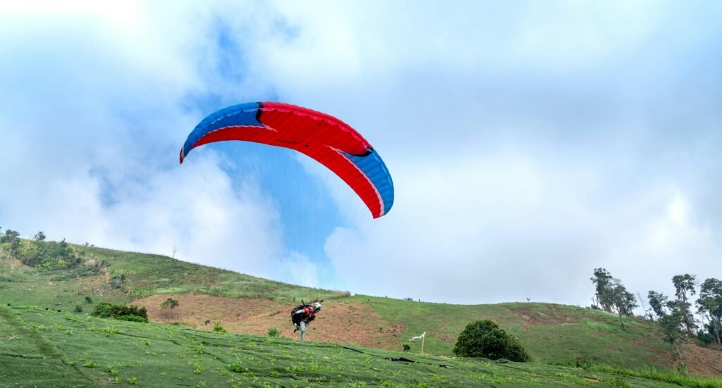 Colorful paraglider soaring over green hills, capturing the thrill of flight and freedom.