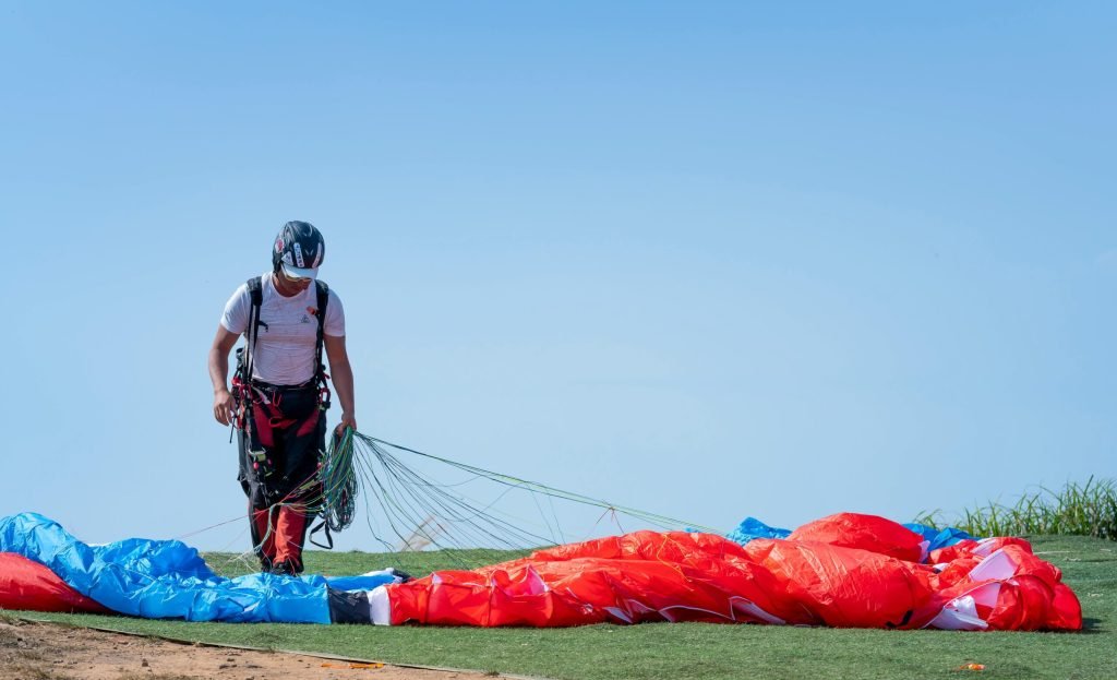 An adult paraglider arranges gear on a sunny day, ready for an outdoor adventure.