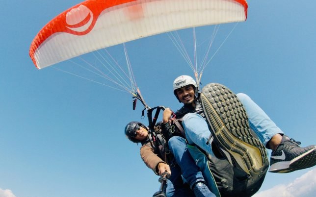 Two men enjoying tandem paragliding against the clear blue sky.