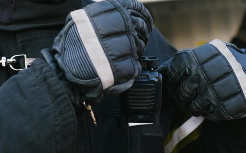 Close-up of a firefighter in turnout gear adjusting a walkie talkie on duty.